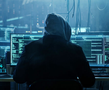 Hooded hacker hacking on various computers
