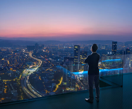 Businessman standing on open roof top balcony watching city night view