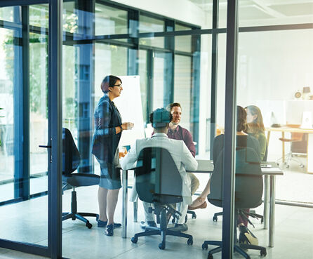 Professionals collaborating in a glass-walled conference room with a bright workspace in the background