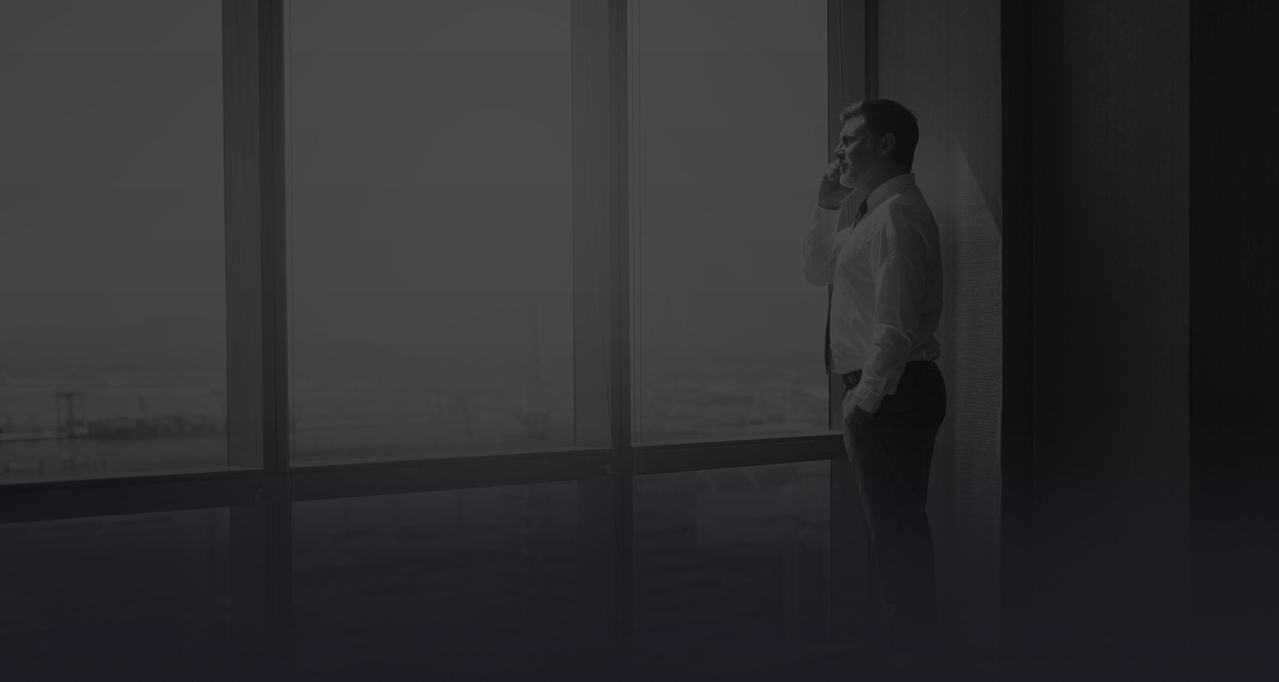 Confident businessman looking out of large windows at a view of the city below while talking on his mobile phone