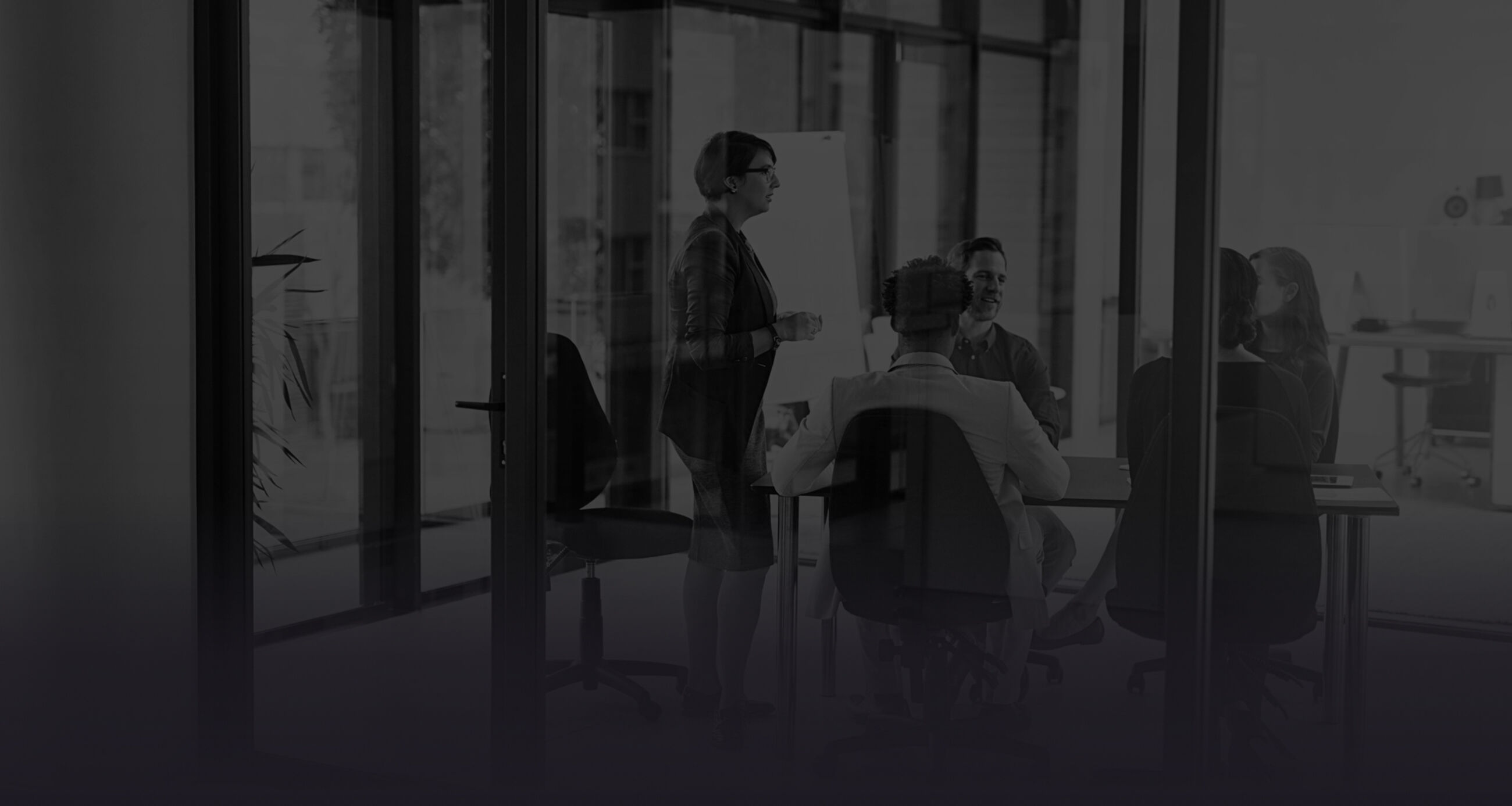 Professionals collaborating in a glass-walled conference room with a bright workspace in the background